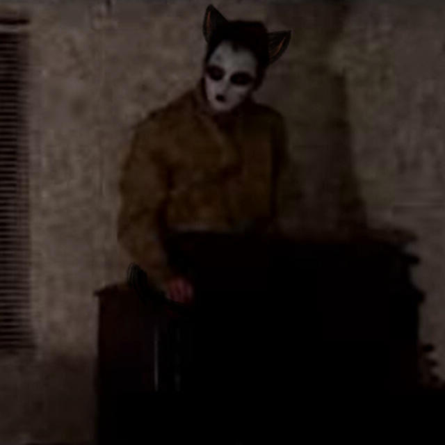 a screenshot of masky from marble hornets sitting on a dresser. cat ears have been drawn onto his head.